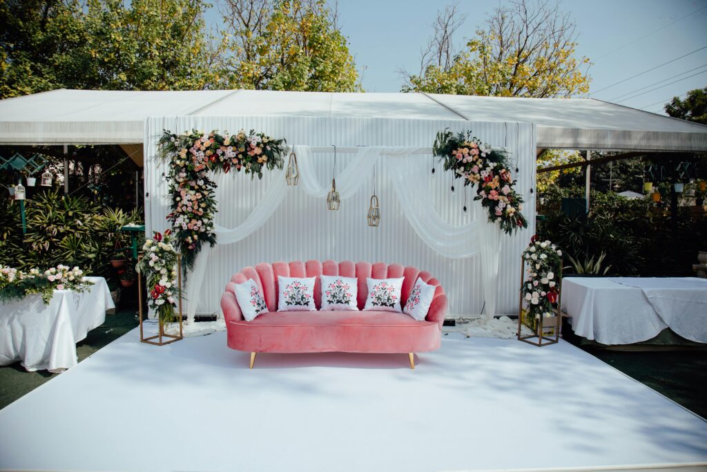 Outdoor wedding setup with floral arrangements, pink sofa, and elegant decor in Gurugram, India.
